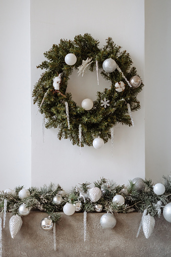 Elegant Christmas decor in a modern interior setting. A lush green wreath adorned with white baubles hangs on a light wall. Concept for holiday interior design inspiration.