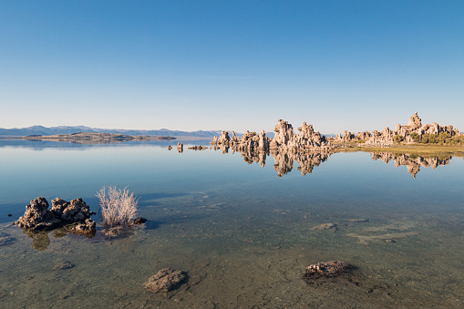 Mono Lake reflecting the Tufa mineral towers and clear blue sky in the arid desert landscape environment of California, USA.