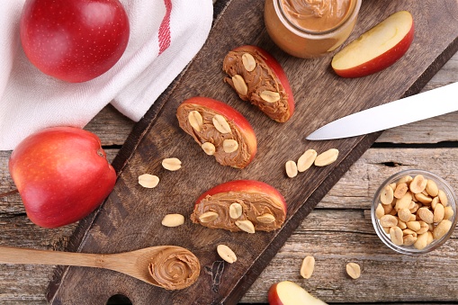 Fresh apples with peanut butter, knife and spoon on wooden table, flat lay