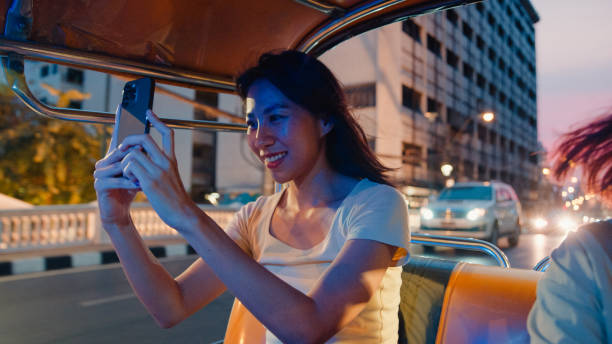 istock Young Asian woman backpack using mobile phone for take a picture while inside a Tuk Tuk vehicle on the street at Bangkok, Thailand. Holiday vacation trip. 1950322572