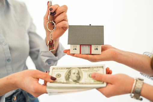 Close-up of a person handing a stack of dollars and a model house to the other person. real estate sale concept
