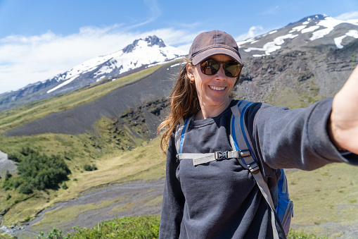 Stunning woman in her 40s capturing a selfie amidst the mountains, solo backpacking adventure.