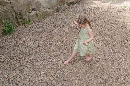 A five-year-old girl walks barefoot on sawdust. She's blonde with two pigtails. Top view.