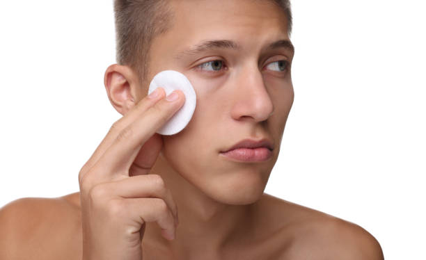 istock Handsome man cleaning face with cotton pad on white background 1950440578