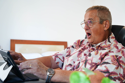 Side view portrait of a surprised man looking at the screen of a digital tablet sitting in the home office
