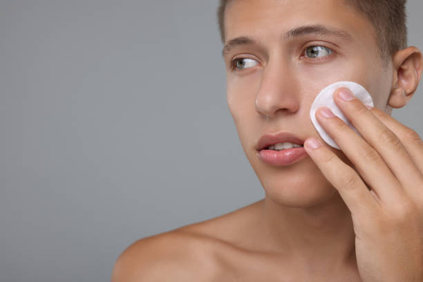 istock Handsome man cleaning face with cotton pad on grey background, space for text 1950441108