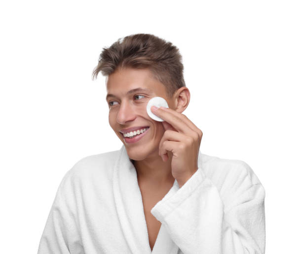istock Handsome man cleaning face with cotton pad on white background 1950441125