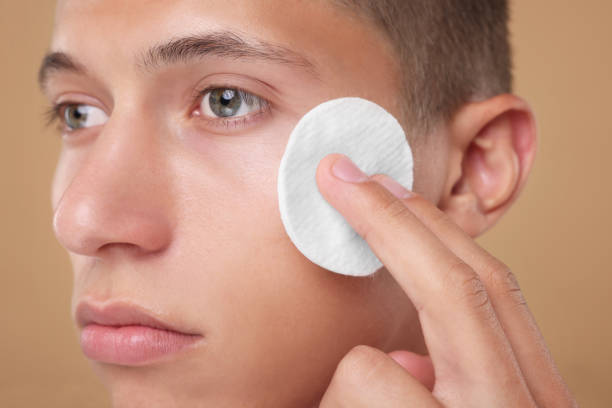 istock Handsome man cleaning face with cotton pad on beige background, closeup 1950443859