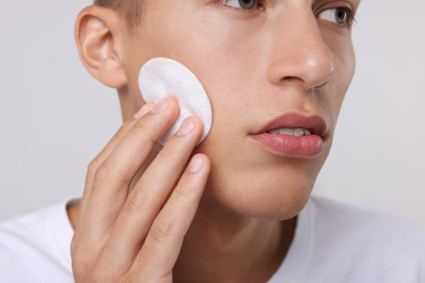 istock Man cleaning face with cotton pad on light background, closeup 1950444671