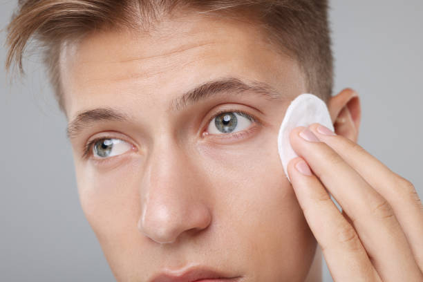 istock Man cleaning face with cotton pad on grey background, closeup 1950446577
