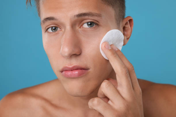 istock Handsome man cleaning face with cotton pad on light blue background 1950446594
