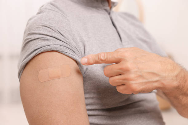 istock Man pointing at adhesive bandage after vaccination against blurred background, closeup 1950462479