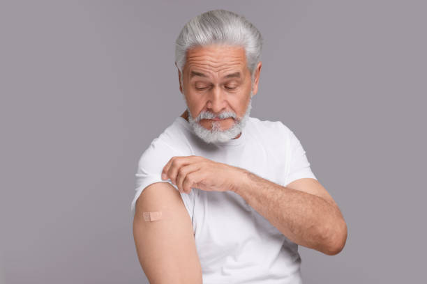 istock Senior man with adhesive bandage on his arm after vaccination against light grey background 1950465164