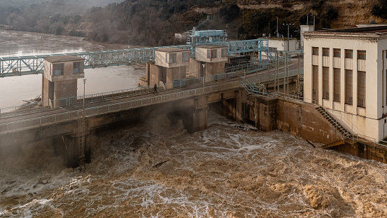 San José reservoir in Castronuño, Valladolid-Spain. Reservoir on the Duero river opening its floodgates due to the increased flow of the river due to the increase of the last rains. Floods. Increased river flow, climate change. Electric power substation, hydroelectric power plant. The river carries with it the remains of dry trees abandoned on the riverbanks.