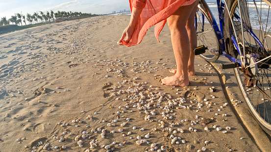 Low angle view of woman pushing bicycle down beach over sand and shells