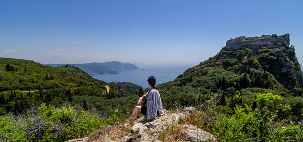Corfu, Greece - May 12 2022: Traveler hiker girl enjoying landscape of Angelokastro in Corfu, Greece from a mountain top during hot summer day