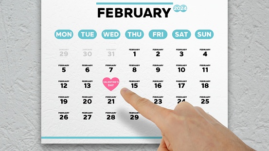 A man's hand points finger to the St Valentine's Day date on a February page 2024 of the wall calendar