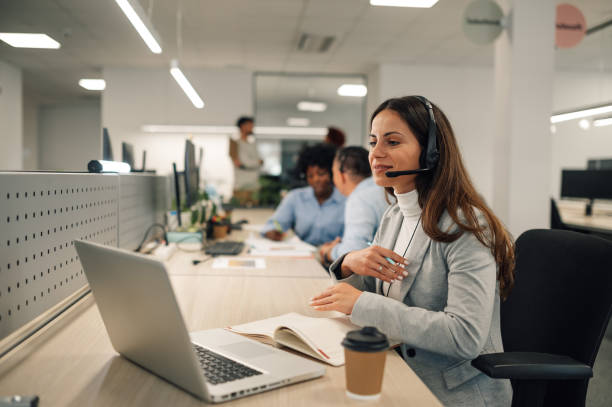 istock Beautiful woman with headset working on a laptop and talking with clients 1950525694
