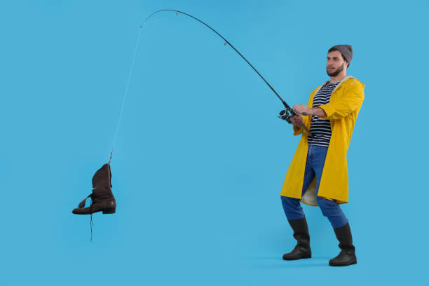 Fisherman with rod and old boot on light blue background