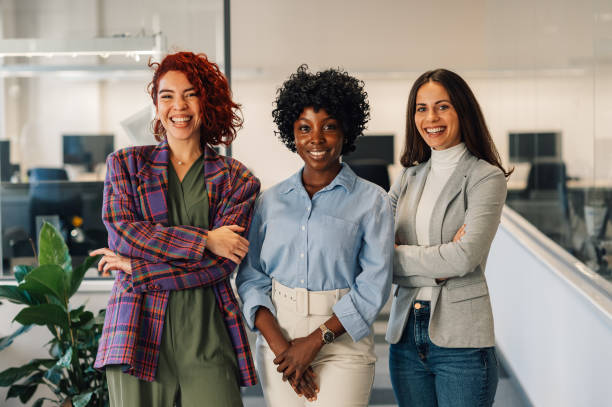 Multiracial women posing in the office while looking into the camera Portrait of a pretty young multiracial businesswomen smiling and standing in the office while looking into the camera. Business woman team leader concept. Diverse business female team. Copy space. only women stock pictures, royalty-free photos & images