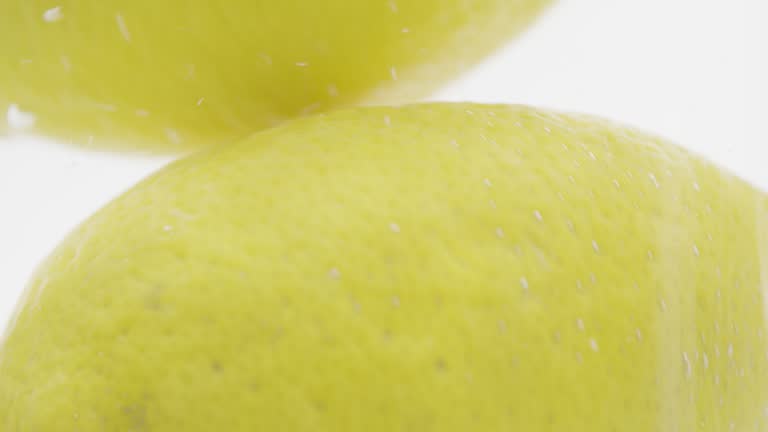 SLO MO LD Whole lemons falling into water against white background