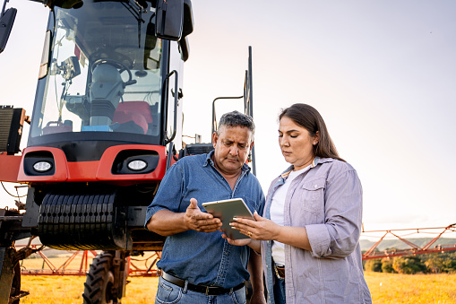 Agronomist and farmer looking at tablet in front of agricultural machine