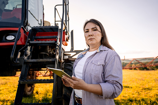 Portrait of female agronomist holding tablet next to agricultural machine