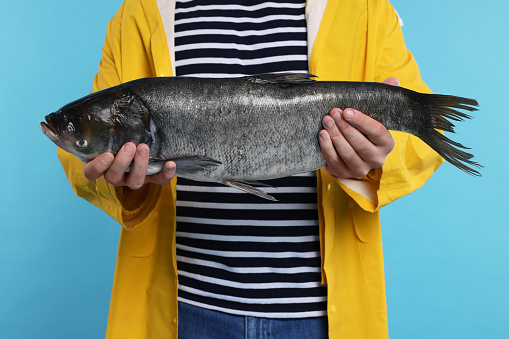 Fisherman with caught fish on light blue background, closeup