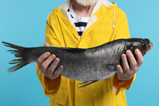 Fisherman with caught fish on light blue background, closeup
