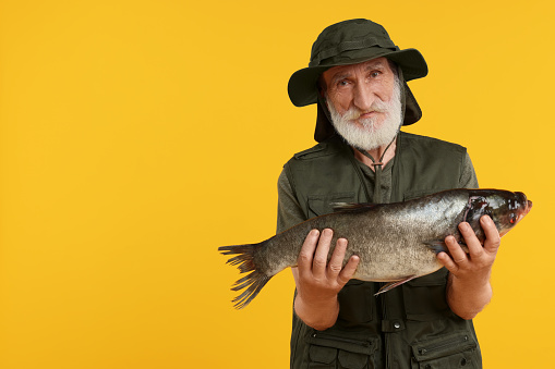 Fisherman with caught fish on yellow background, space for text