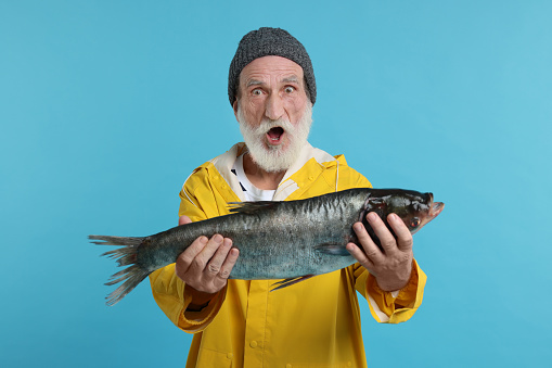 Shocked fisherman with caught fish on light blue background