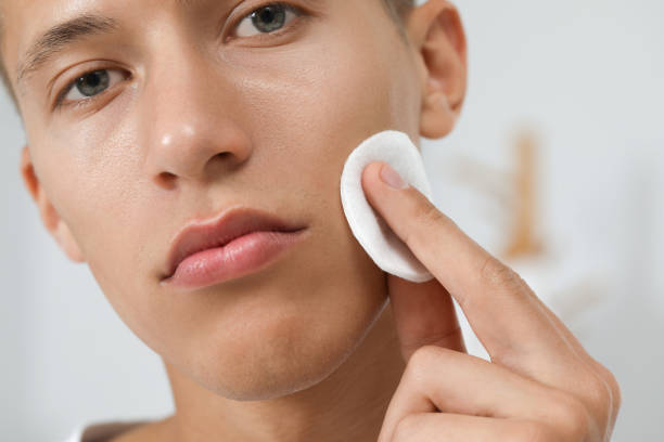 istock Handsome man cleaning face with cotton pad against blurred background, closeup 1950576427