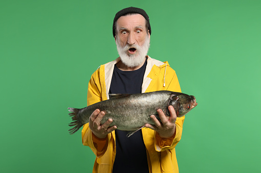 Shocked fisherman with caught fish on green background