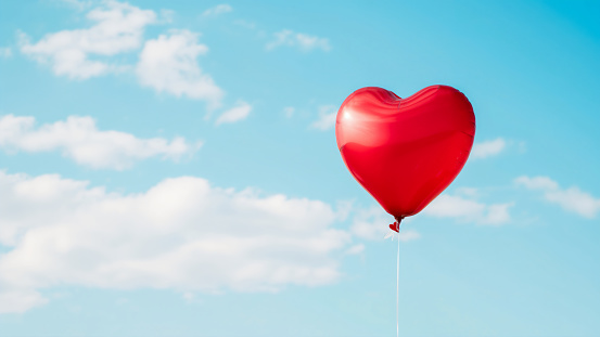 Red heart shaped balloon in blue sky.