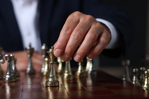 Man moving chess piece on checkerboard against dark background, closeup