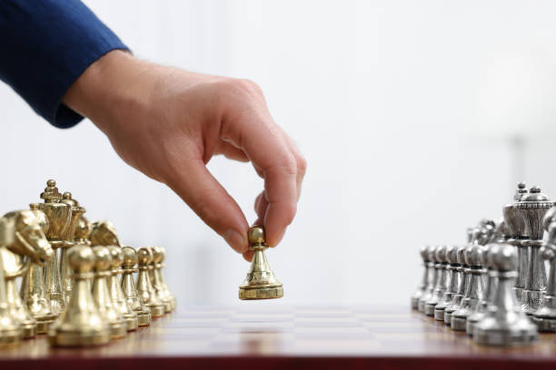 istock Man with game piece playing chess at checkerboard against white background, closeup 1950602589