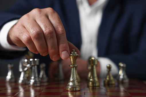 Man moving chess piece on checkerboard against dark background, closeup
