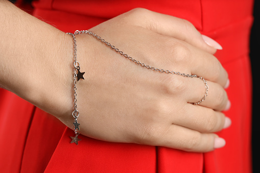 Woman wearing stylish metal chain with pendants and ring on her hand, closeup. Luxury jewelry