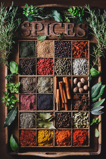 A large selection of commonly used spices in wooden bowls on an old vintage tray. Decorated with green fresh herbs