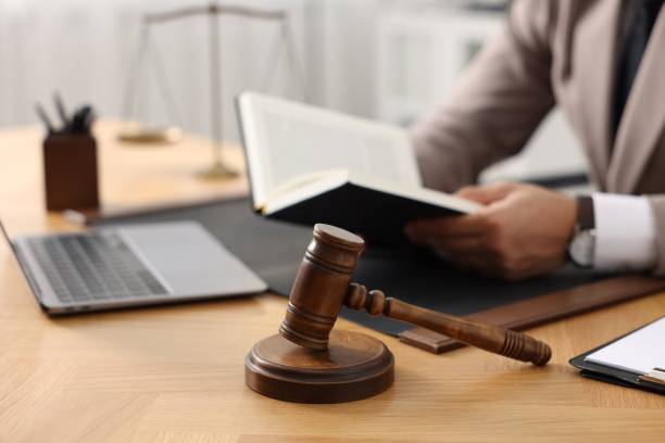 istock Lawyer reading book at table in office, focus on gavel 1950624245