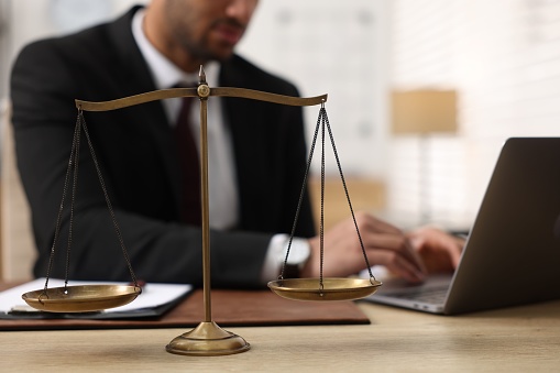 Lawyer working with laptop at table in office, focus on scales of justice