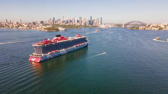 Aerial drone view of Resilient Lady Virgin Voyages cruise ship at Athol Bay in Sydney Harbour, NSW, showing Sydney City in the background on a sunny day in January 2024