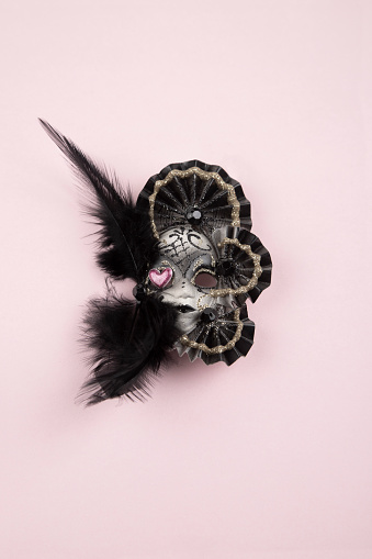 Mask decorated with feathers and heart isolated on pink background