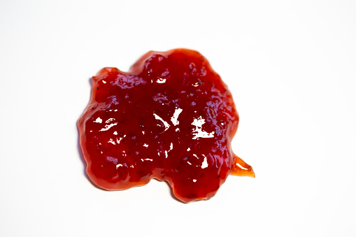 A red drop of juicy strawberry jam on a white background.