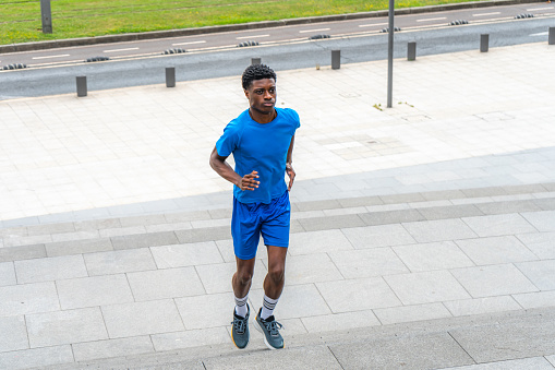 Ready for the challenge: Medium shot of a young man, clad in blue sportswear, climbing stairs. His determined expression reveals an active warm-up before the workout.