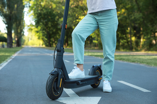Woman with modern electric kick scooter in park, closeup