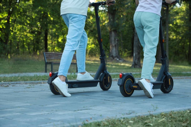 istock Couple riding modern electric kick scooters in park, back view 1950784136