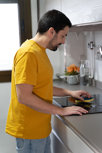A man wearing a yellow shirt is seen concentrating as he works on his laptop.