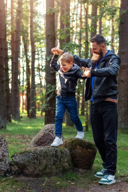 istock A cheerful active boy in a sunny pine forest during a walk with his father. A father holds his son's hands and teaches him to rock climb while keeping his balance. 1950937328