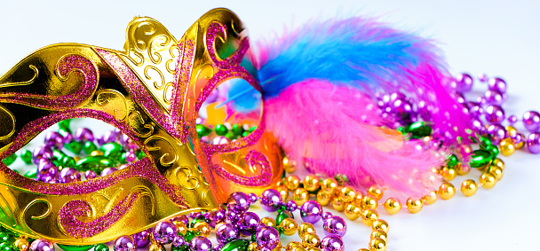 Golden carnival mask and colorful beads on white background. Closeup symbol of Mardi Gras or Fat Tuesday. Holiday decorations in gold, green and purple. Banner format